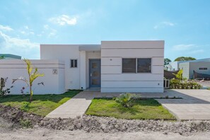 Ein modernes, zweistöckiges Haus mit flachem Dach, einer Haustür und einer kleinen Veranda.