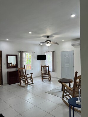 A spacious room with a ceiling fan, a flat-screen TV mounted on the wall, and a door.