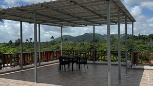A covered outdoor area with a tiled floor, a table with chairs, and a view of green hills in the background. - 3 Bedroom Country Villa with Private Pool (El Bonao)