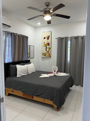 Un dormitorio con cama, ventilador de techo, un cuadro y cortinas.