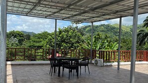 A covered outdoor patio with a table and chairs, surrounded by a metal railing and a view of a hilly landscape. - 3 Bedroom Country Villa with Private Pool (El Bonao)