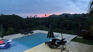 A swimming pool with lounge chairs and umbrellas, surrounded by lush greenery and hills in the background. - 3 Bedroom Country Villa with Private Pool (El Bonao)