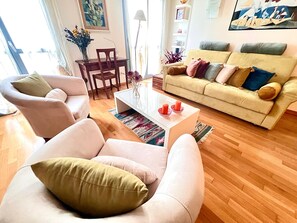 A living room with a sofa, armchairs, a coffee table, and a dining area with a table and chairs. - Casa ai Giardini 2 NEL CUORE DEL CENTRO STORICO (LUCCA)