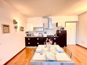 A compact kitchen with a dining area, featuring a microwave, stove, and cabinets. - Casa ai Giardini 2 NEL CUORE DEL CENTRO STORICO (LUCCA)