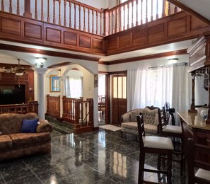 A spacious living area with a high ceiling, wooden staircase, a television, a sofa, and a dining area with chairs and a table. - Sukasa Ville 3 beautiful bedroom
Perfect for family
The villa edition (Trelawny)