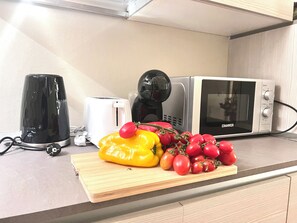 A kitchen counter with a toaster, a coffee maker, a microwave, and a cutting board with tomatoes and a bell pepper. - Liù, Central and cozy apartment in Lucca (LUCCA)