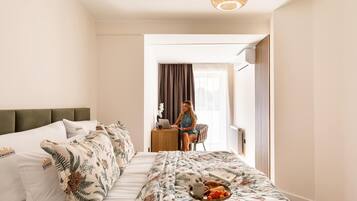 A hotel room with a bed, a desk, and a person working on a laptop.
