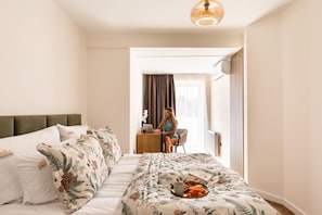 Hotellihuone, jossa on sänky, työpöytä ja henkilö, joka työskentelee kannettavan tietokoneen parissa.