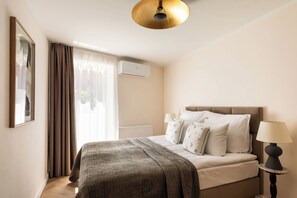 A hotel room with a bed, a bedside table, a lamp, a window with curtains, and an air conditioning unit. - Kraków Bohaterów Września 10 | AC | Parkside (Kraków)