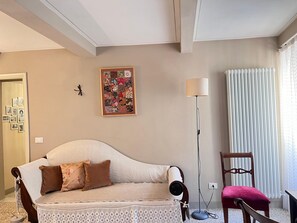 A room with a sofa, a chair, a floor lamp, a wall with a framed picture, and a door with pictures on the wall. - Casa Albertina central/ac 2/bathrooms (LUCCA)