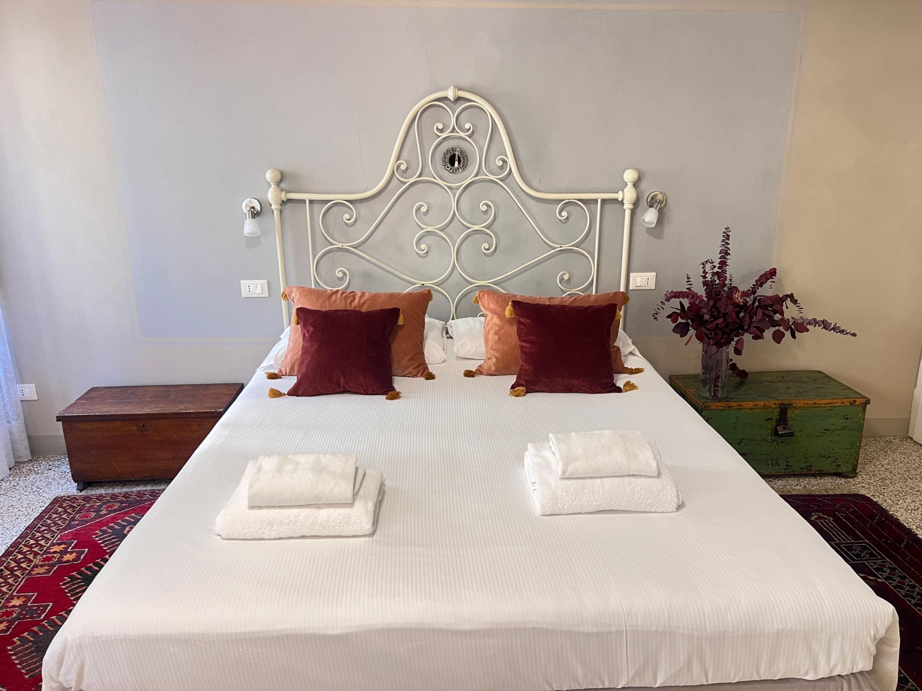A neatly made bed with a metal headboard, two pillows, and two folded towels.