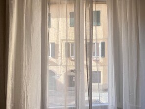 A window with sheer white curtains, a view of a building with multiple windows and shutters. - Casa Albertina central/ac 2/bathrooms (LUCCA)