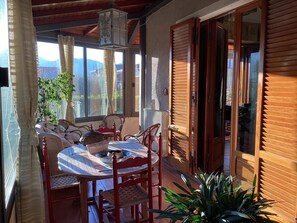 A sunlit patio with a round table and chairs, a potted plant, and wooden shutters. - Mansarda in Villa Riccardo (BARGA)