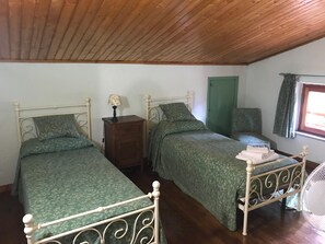 Ein Schlafzimmer mit zwei Einzelbetten, einer Holzkommode, einer grünen Tür und einem Fenster mit Vorhängen.