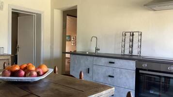 A kitchen with a wooden table, a bowl of fruit, a modern oven, and a stainless steel faucet.