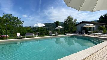 A swimming pool with lounge chairs and umbrellas, surrounded by greenery and a mountain view.
