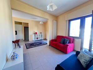 Ein Wohnzimmer mit einem roten Sofa, einem blauen Sofa, einem weißen Konsolentisch, einem gemusterten Teppich und einem großen Fenster.