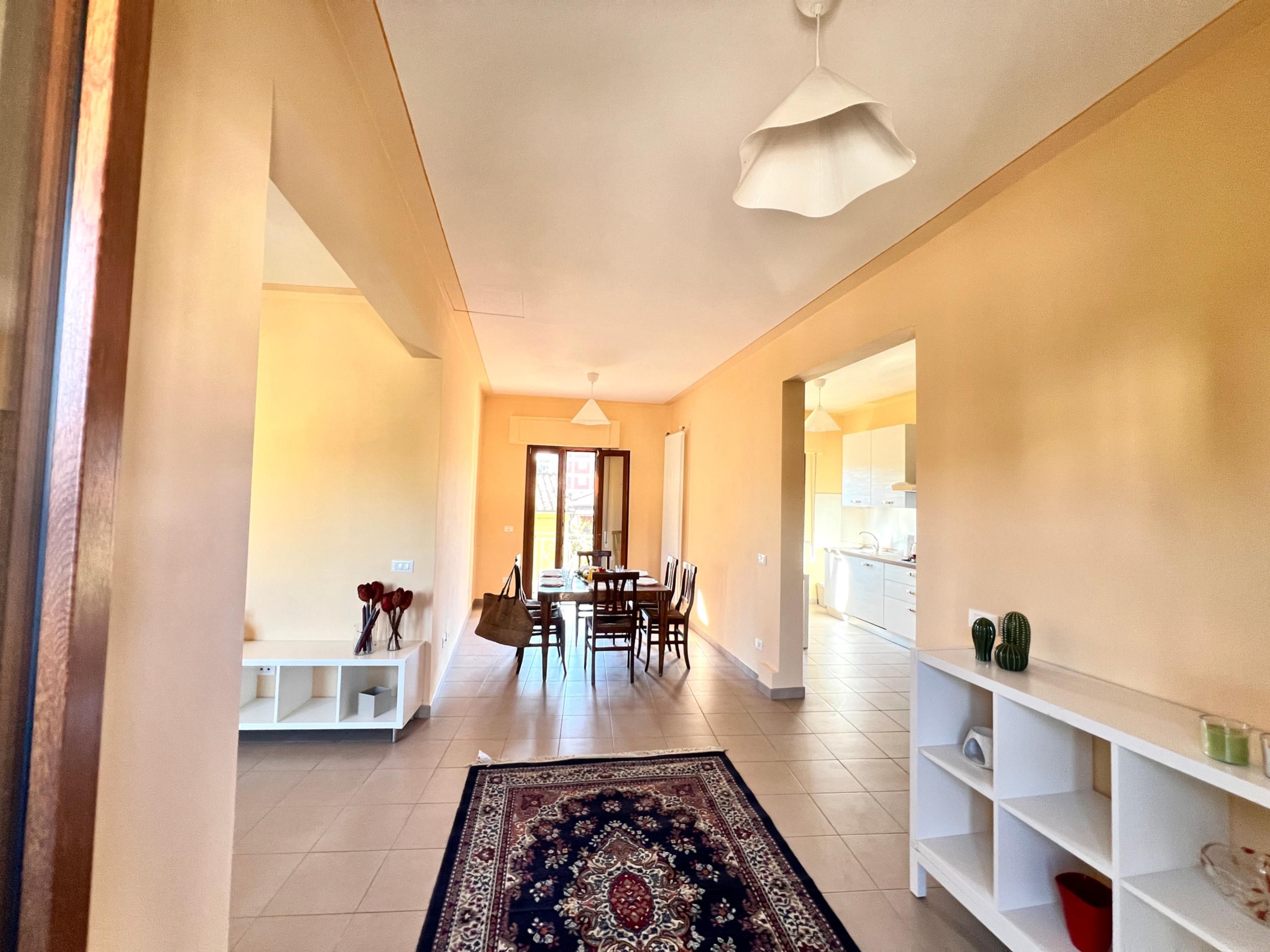 A hallway with a dining area, white shelves, and a patterned rug.