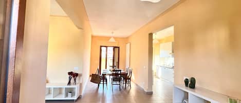 A hallway with a dining area, white shelves, and a patterned rug.