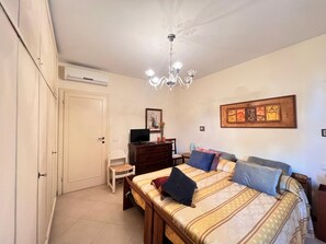 Une chambre à coucher comprenant un lit, une commode, une chaise, un téléviseur et un ventilateur de plafond.