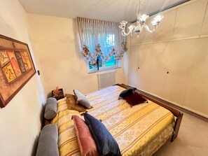 Ein Schlafzimmer mit einem Bett, einer Chandelüster, einem Fenster mit Vorhängen und einer Heizung.
