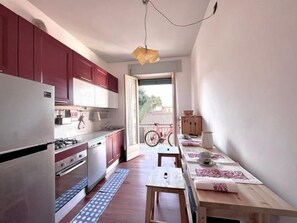 Une cuisine compacte équipée d’un réfrigérateur, d’une cuisinière et de placards, donnant sur un balcon où se trouve un vélo.