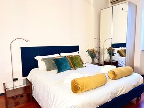 Un lit bien fait, avec une tête de lit bleue, une literie blanche et plusieurs oreillers de différentes couleurs.