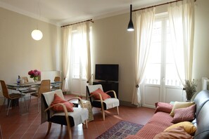 Ein Wohnzimmer mit einer Couch, Sesseln, einem Esstisch und einem Fernseher.