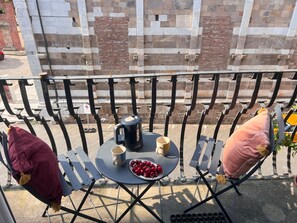 Ein Balkon mit einem Tisch für zwei Personen, einem Wasserkocher, einer Tasse und einer Schale voll Kirschen.