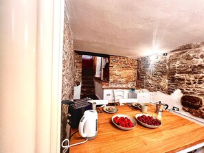Une cuisine rustique avec des murs en pierre, un plan de travail en bois et une bouilloire.