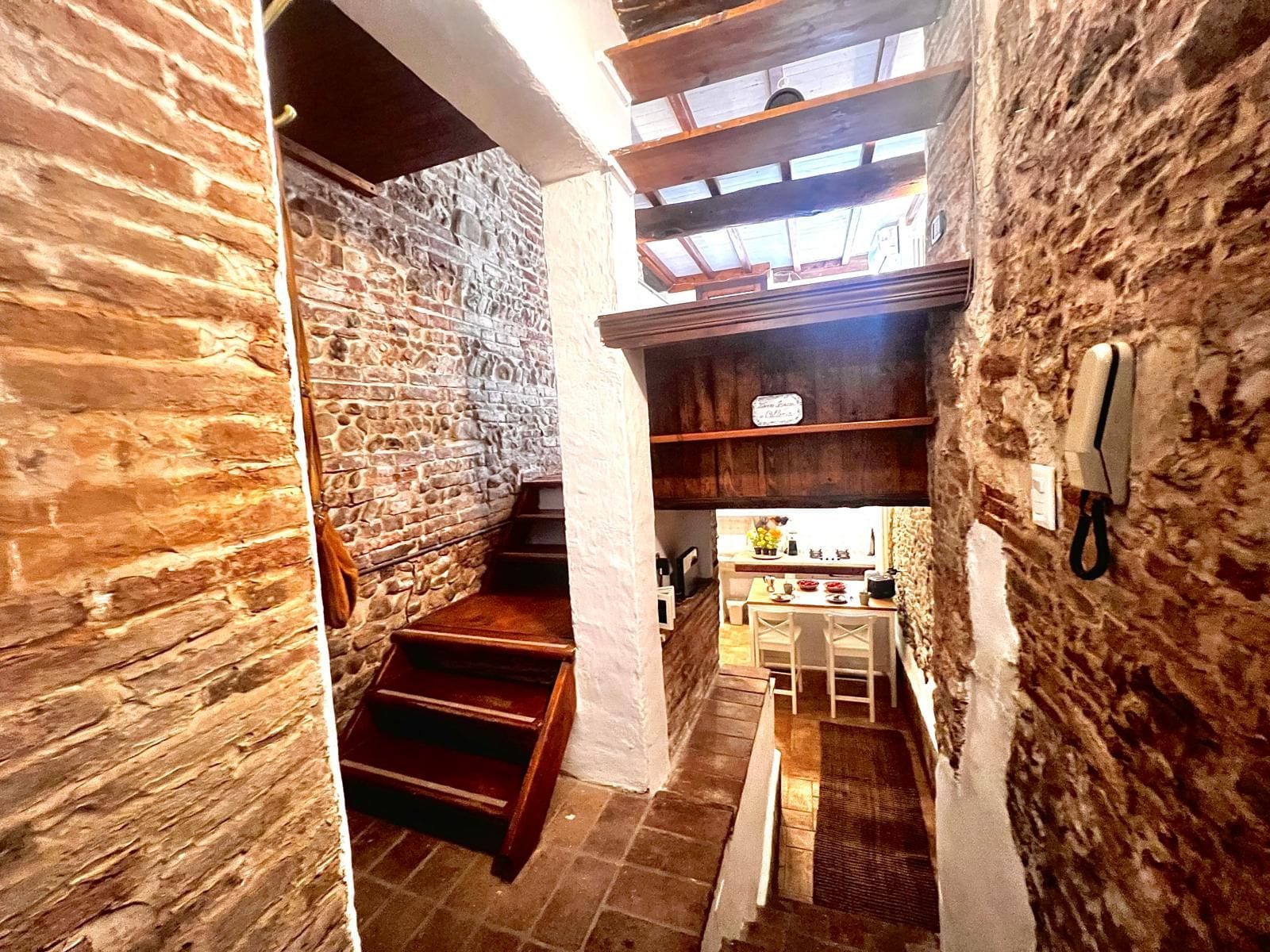 Una escalera estrecha conduce a una cocina con paredes de piedra y vigas de madera.