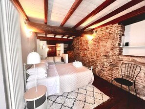 Une chambre avec un mur en pierre, un lit avec une literie blanche, une table ronde et une chaise.
