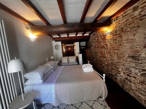 A bedroom with a bed, bedside tables, a lamp, and a stone wall. - Casa in Pelleria nel cuore del centro storico (LUCCA)