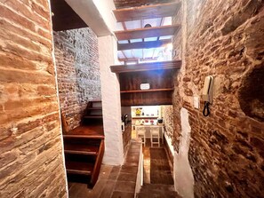 A narrow stone-walled corridor with wooden steps leading to a room with a table and chairs. - Casa in Pelleria nel cuore del centro storico (LUCCA)