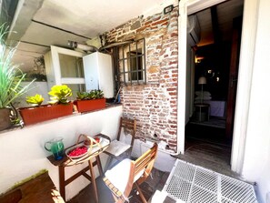 A room with a brick wall, a window, a wooden chair, a table with a pitcher and a basket of fruit, and a potted plant. - Casa in Pelleria nel cuore del centro storico (LUCCA)