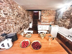 A rustic kitchen with a wooden table set for two, a kettle, and bowls of fruit. - Casa in Pelleria nel cuore del centro storico (LUCCA)