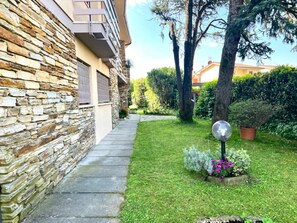 Un bâtiment en pierre doté d’un balcon, d’un chemin pavé et d’un jardin bien entretenu, agrémenté d’un lampadaire et de plantes en pot.
