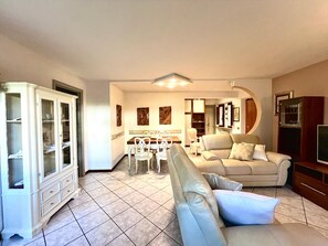 Een woonkamer met een bank, een eettafel met stoelen, een kast en een televisie.