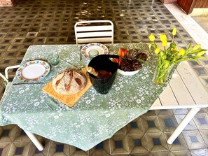 Een gedekte tafel met een bloemenloper, een brood, een fruitschaal, een vaas met bloemen en een bord met een kopje.