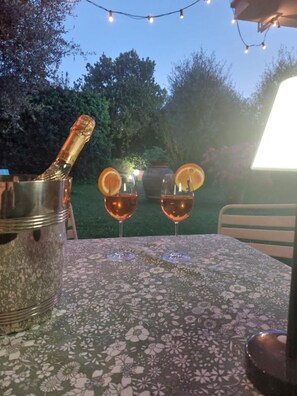 Une table recouverte d’une nappe à motifs floraux, deux verres contenant un liquide ambré et un récipient en métal.