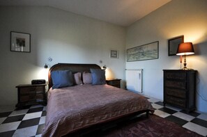A bedroom with a bed, two bedside tables, a dresser, a radiator, and a checkered floor. - Casa il Tiglio nel cuore delle colline lucchesi (LUCCA)
