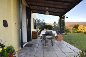 An outdoor patio with a table and chairs, a hanging light fixture, and a view of a garden and hills. - Casa il Tiglio nel cuore delle colline lucchesi (LUCCA)