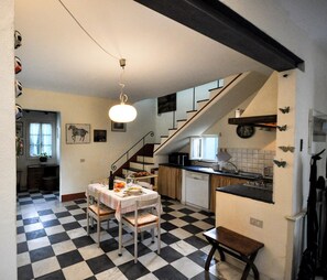 A compact kitchen with a checkered floor, a dining table with chairs, a staircase, and a hanging light fixture. - Casa il Tiglio nel cuore delle colline lucchesi (LUCCA)