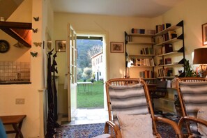 A cozy living room with a view of a garden, a bookshelf, and a dining area. - Casa il Tiglio nel cuore delle colline lucchesi (LUCCA)