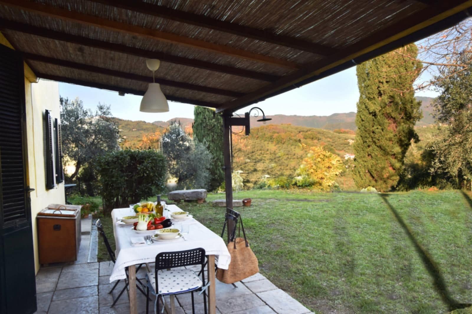 An outdoor dining area with a table set for two, a chair, and a hanging light fixture.