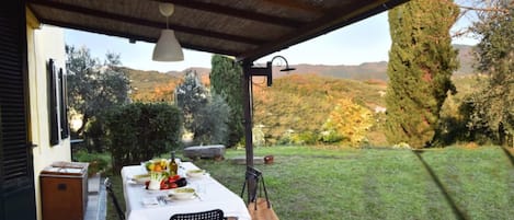 An outdoor dining area with a table set for two, a chair, and a hanging light fixture.