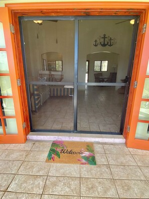 A hotel entrance with a sliding glass door, a reception area visible through the door, and a welcome mat at the entrance. - Lovely 2BR Villa Plus a New Pool-Stunning Views of St. Maarten (George Hill)