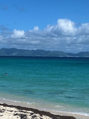 A beach with clear turquoise water, a sandy shore, and distant mountains under a partly cloudy sky. - Lovely 2BR Villa Plus a New Pool-Stunning Views of St. Maarten (George Hill)
