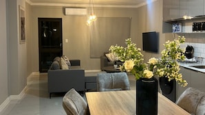 A modern living room with a dining table, sofas, and a kitchen in the background. - Sandton Wespoint Luxury Apartments (Sandton)
