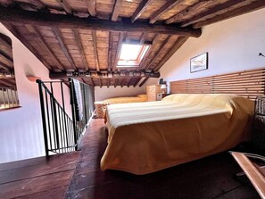 A bedroom with a wooden ceiling, a bed with a yellow bedspread, a wooden headboard, a nightstand, and a window with a view. - Casa Silvia a piedi dalle mura AC (LUCCA)